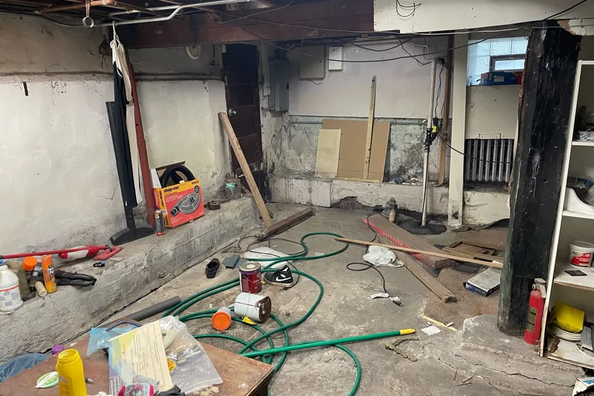 Cluttered unfinished basement with hoses and debris before a basement cleanout by ONIT Junk Removal